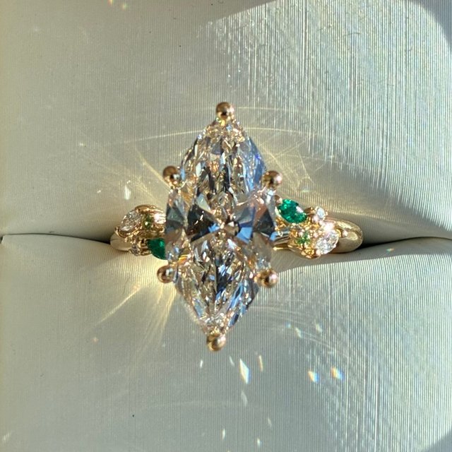 For the one who loves a touch of color. The details: 18K Yellow Gold Arden Diamond Ring with Lab Emerald Accents set with a Marquise Diamond